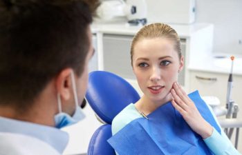 A young woman looks at the dentist and touches her cheek.