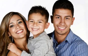 The Spanish family is smiling. Mom and dad are holding a child in their arms.