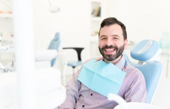 Jouful middle-aged man with a perfect smile sitting in a dental chair after treatment.