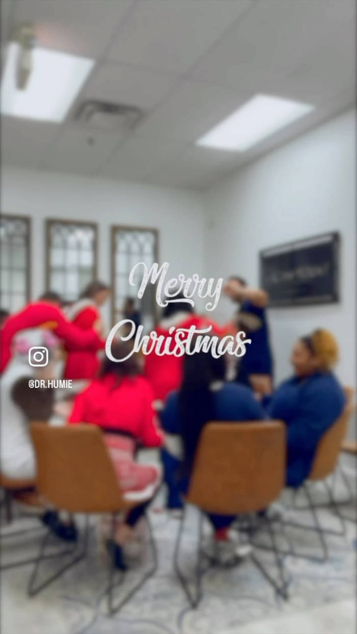 Blurred office or meeting room scene with people in red and blue clothing sitting at a table, overlaid with 'Merry Christmas' text and an Instagram camera icon.