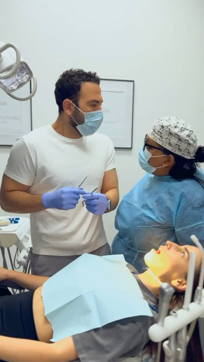 Dental procedure in progress with masked dentist and assistant treating a patient in a dental chair in a clinical setting.