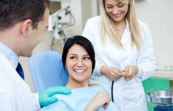 A dentist and a dental technician talking to a satisfied relaxed woman sitting after treatment in a dental chair.