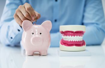 Man putting a coin into a piggy money bank standing next to a dental model.