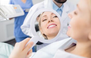 A happy woman sitting in a dental chair after a treatment looking at her teeth and gums in a mirror.