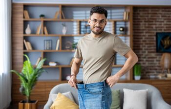 Happy man after bariatric weight loss procedure wearing his old oversized jeans to show the difference in his body size and shape