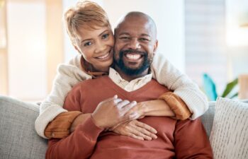 A happy Afro-American senior couple with perfect smiles posing at the photo sitting on the sofa and smiling broadly